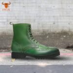 Green leather brogue boots with decorative perforations on pavement