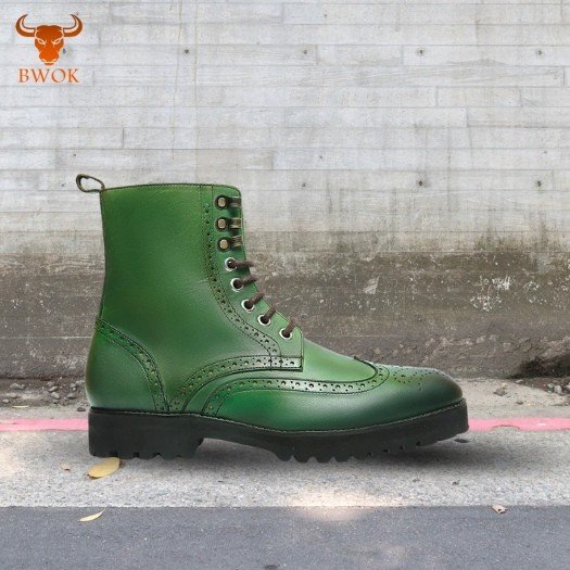 Green leather brogue boots with decorative perforations on pavement