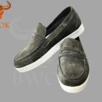 Pair of suede grey men’s loafers with white soles on grey background