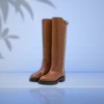 Pair of long brown horse riding boots on a light blue background