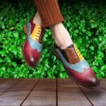 Person wearing colorful leather Oxford shoes standing on wooden floor with green background