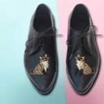 Black women’s leather loafers with gold beaded embroidery on pastel background